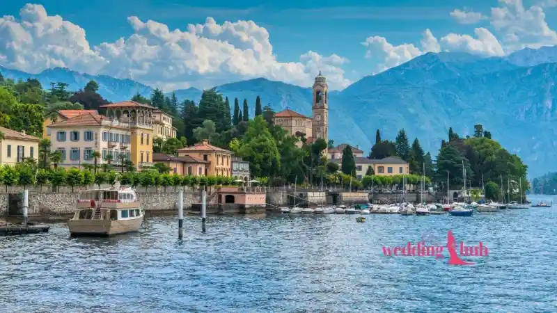 A bride in a white wedding gown and groom in a tuxedo walking through the elegant garden of a luxury villa on Lake Como with mountain views.
